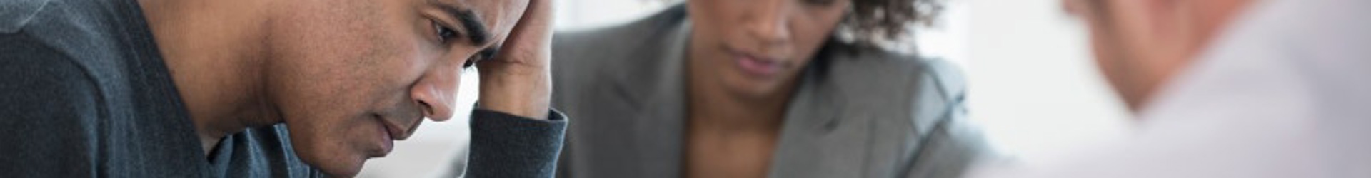 Man at a table with colleagues, appearing frustrated while working on ASD Essential Eight cybersecurity strategies.