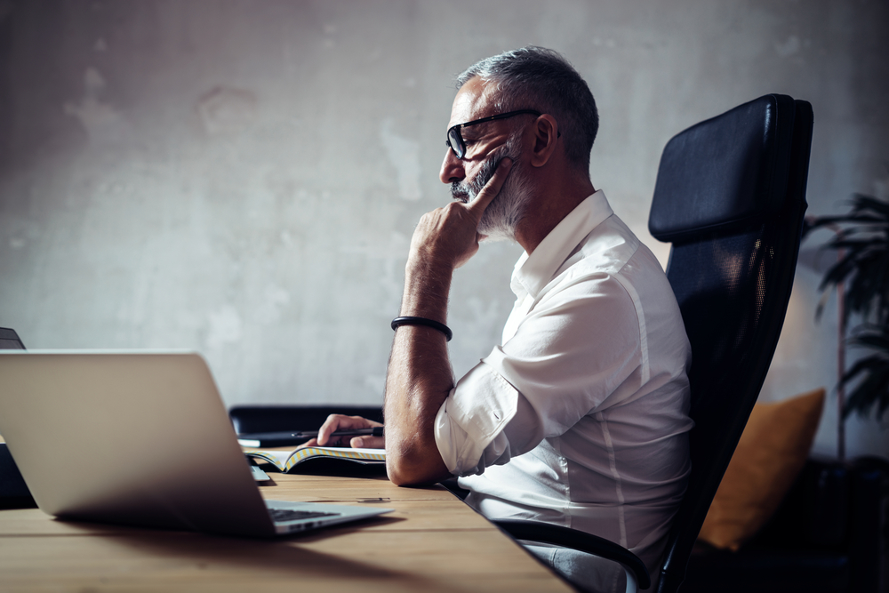 CEO sitting at a desk with a pen and notebook looking at the Policy Management as a Service offering 